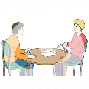 Ein Mann und eine Frau mit heller Hautfarbe sitzen an einem Tisch. Die Frau gebärdet. Auf dem Tisch liegen Zettel.