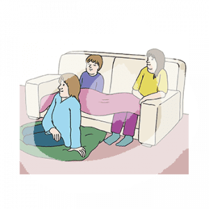 Zwei Kinder sitzen unter einer Decke auf dem Sofa, davor sitzt eine Frau auf einer Decke.