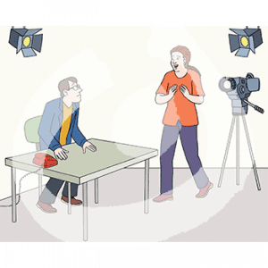 Eine Person sitzt an einem Tisch. Darauf steht ein Telefon. Zwei Scheinwerfer hängen an der Decke. Eine weitere Person steht klatschend vor einer Kamera.