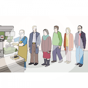 Eine Person in Schürze steht vor einem Standbohrer .Sie hält das zu bohrende Teil mit einem Handschuh fest. Im Hintergrund stehen fünf Personen und gucken zu. Eine Person trägt einen Kittel.