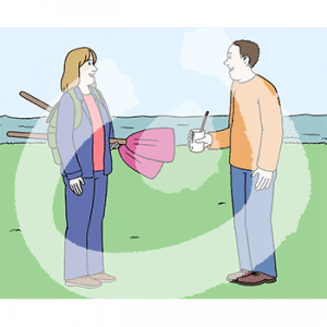 Eine Person hat Paddel unterm Arm. Vor ihr steht eine andere Person mit einem Becher in der Hand. Im Hintergrund das Meer.