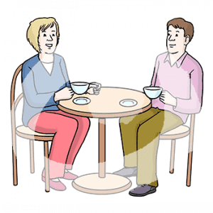 Zwei Personen sitzen sich mit Tassen an einem Tisch gegenüber.