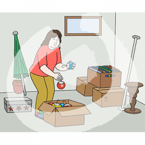 Eine Person steht in einem Raum mit einem kleinen Fenster. Sie hat Weihnachtsbaumkugeln in der Hand und steht vor einem Karton. Dahinter stehen Kisten, Kartons und weitere Gegenstände.