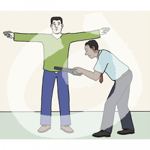 Eine Person steht mir ausgebreiteten Armen neben einer Person in Uniform. Sie hält einen Metalldetektor in den Händen.