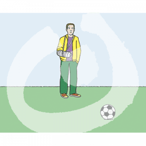 Ein Mann in Trainingsjacke und Gips Arm steht vor einem Fußball auf Gras.