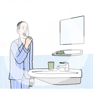 Ein Mann im Schlafanzug steht Zähne putzend vor einem Waschbecken.