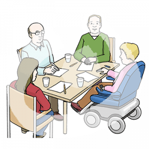 Vier Personen sitzen um einen Tisch herum. Vor jeder liegt ein Blatt und ein Stift. Eine Person sitzt im Rollstuhl.