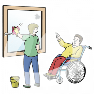 Eine Person sitzt im Rollstuhl und zeigt auf einen Fleck auf einem Fenster. Eine andere Person putzt das Fenster.