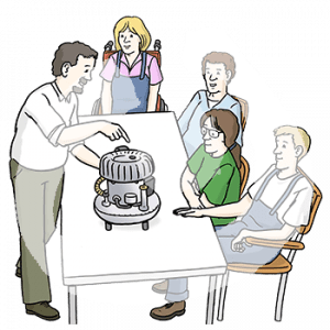 Vier Personen sitzen an einem Tisch. Davor steht eine Person und zeigt auf ein Gerät.