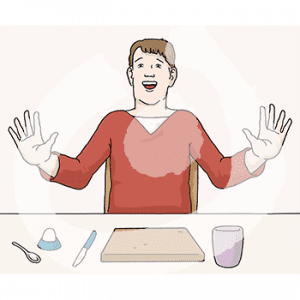 Eine Person sitzt an einem Tisch mit Brett, Messer und Becher und hält die Hände vor sich.