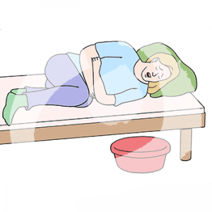 Eine Person liegt mit geschlossenen Augen in einem Bett und hält sich den Bauch. Neben dem Bett steht eine Schüssel.