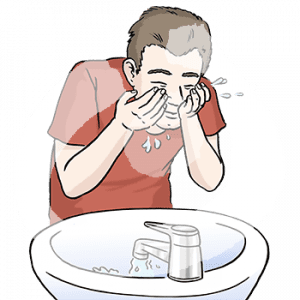 Eine Person steht vor einem Waschbecken mit laufendem Wasserhahn. Sie wäscht sich mit beiden Händen das Gesicht.