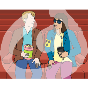 Zwei Personen sitzen auf roten Sesseln. Eine Person hat Popcorn in der Hand, die andere hat eine Sehbehindertenbinde und ein Handy mit Kopfhörern.
