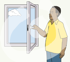 Eine Person steht mit dem Fenstergriff in der Hand neben einem weit offenen Fenster.