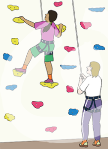 Eine Person in Sicherheitsgurt hält sich an einer Kletterwand fest. Unter ihr steht eine andere Person in Sicherheitsgurt und hält sie am Seil fest.