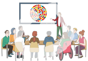 Eine Gruppe von Menschen sitzt U-förmig an Tischen und guckt zu einer großen Leinwand. Eine Person zeigt etwas darauf. Auf der Leinwand sind kleine Kreise innerhalb eines großen Kreises zu sehen.