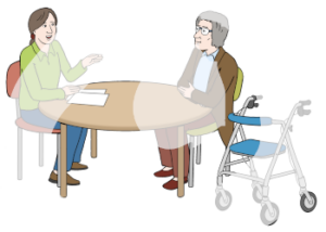 Zwei Personen sitzen an einem Tisch. Eine Person ist älter und hat neben sich einen Rollator stehen. Die andere Person ist jünger und hat vor sich zwei Zettel auf dem Tisch liegen.