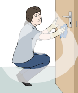 Eine Person hockt mit einem Lappen in der Hand vor einer Tür. Sie hält den Lappen an die Tür.