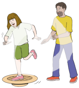 Eine Jugendliche steht auf einem Bein auf einem Balancetrainer. Dahinter steht ein Mann mit vorgestreckten Armen.