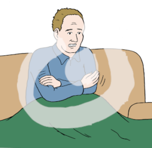 Eine Person sitzt auf dem Sofa. Die Person hat über ihre Beine eine Decke gelegt. Sie hat die Arme über dem Oberkörper verschränkt und zittert.