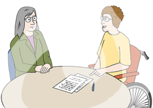 Zwei Frauen sitzen an einem Tisch. Eine Frau sitzt im Rollstuhl. Sie zeigt auf ein aufgeschlagenes Heft auf dem Tisch.