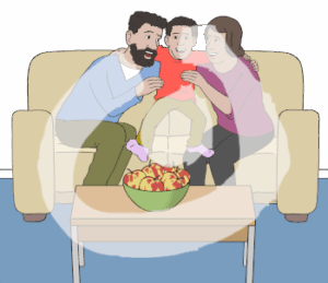 Mann und Frau sitzen auf Sofa. Zwischen ihnen sitzt ein Junge. Er legt die Arme um ihre Schultern. Mann und Frau legen auch die Arme um seine Schultern. Alle lachen. Auf einem Tisch steht eine Schale Äpfel.